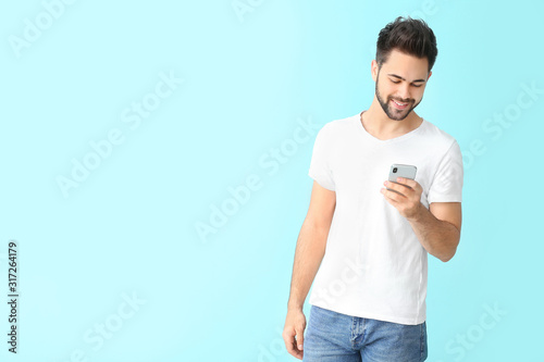 Happy young man with mobile phone on color background