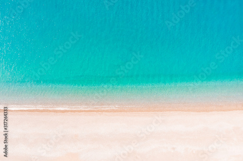 Flying over an empty sandy beach and beautiful emerald ocean waves. Top view landscape scene of waves rolling on an empty tropical beach
