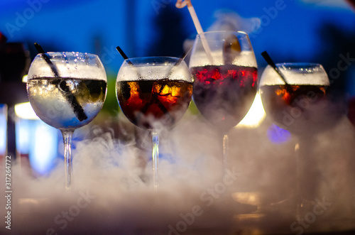 Beautiful row line of different colored alcohol cocktails on a party, martini, vodka,and others on decorated catering bouquet table on open air event, picture with beautiful bokeh