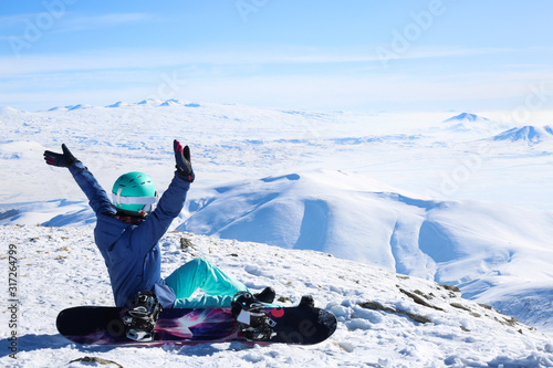 Happy young sportive woman sitting with hands up at the top of the mountain Tegenis in Tsaghkadzor ski resort Armenia.