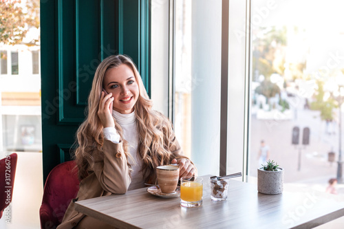 Beautiful business woman sitting in modern city cafe and talking by phone while drinking coffee.