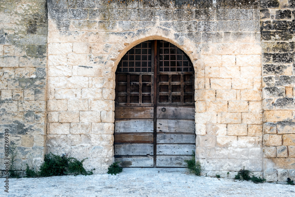 Wooden door with bars and an arch in a stone wall. Monopoli, Italy.