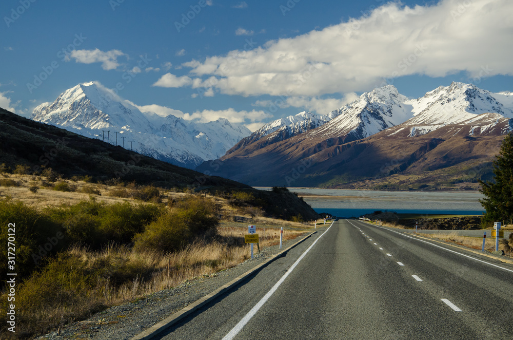 Snow covered Mount Cook with road in the foreground amd blue sky and white clouds, South Island, New Zealand
