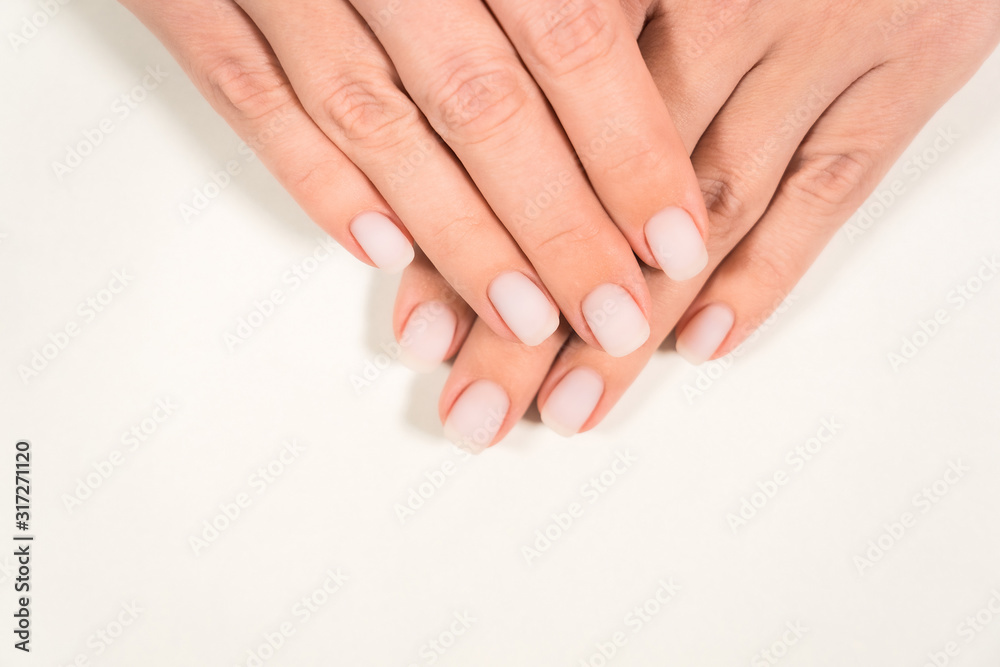 Closeup top view color photography of two beautiful female hands with modern trendy pastel natural manicure naildesign covered with finish mat top without glance. 