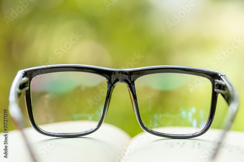 Book and eye glasses on wooden table with abstract green nature blur background. Reading and education concept