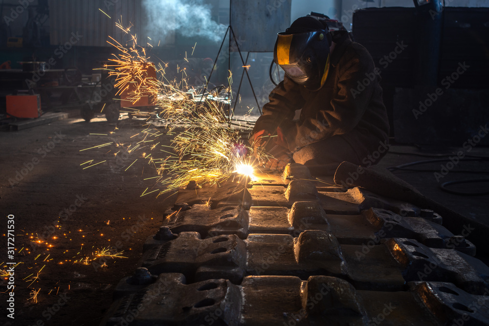 Side view of welder in protective helmet welding metal detail with sparks at factory Side view of welder in protective helmet welding metal detail with sparks at factory