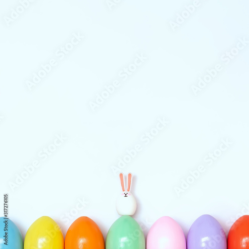 Top view of an Easter composition of painted eggs in bright juicy colors on a white background with a little rabbit. Holiday concept, flat layout, minimalism.