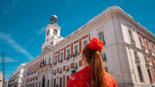 A young caucasian woman chulapa with red flower, traditional dress, and Spanish scarf at Puerta del Sol during San Isidro, the spring festival in May in the downtown of Madrid, the capital of Spain photo