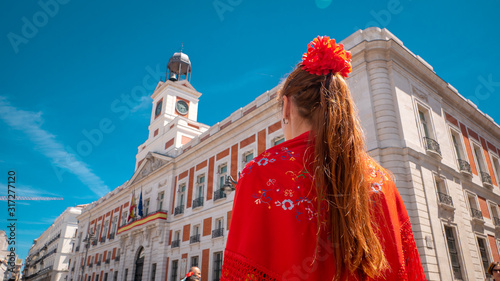 A young caucasian woman chulapa with red flower, traditional dress, and Spanish scarf at Puerta del Sol during San Isidro, the spring festival in May in the downtown of Madrid, the capital of Spain photo