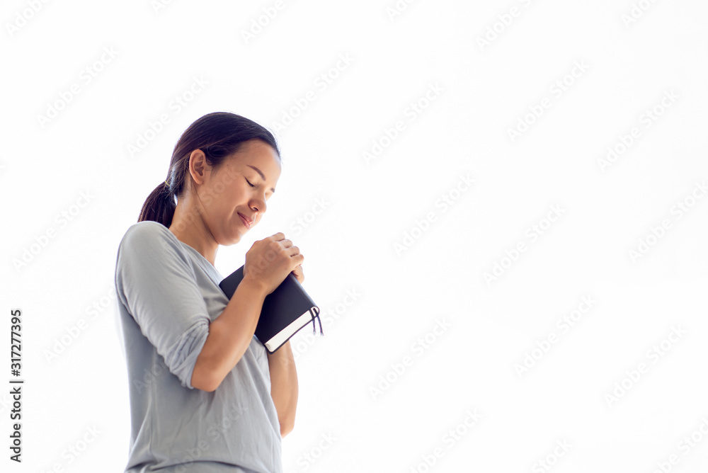 Asian woman close her eyes holding bible book hands folded praying on white bacground Asian woman close her eyes holding bible book hands folded praying on white bacground