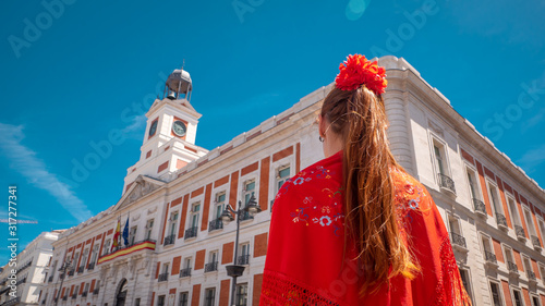 A young caucasian woman chulapa with red flower, traditional dress, and Spanish scarf at Puerta del Sol during San Isidro, the spring festival in May in the downtown of Madrid, the capital of Spain