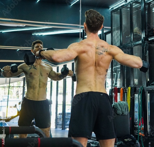 Caucasian Shirtless Tattooed Man Exercising Using Dumbbell Should Flys in Mirror