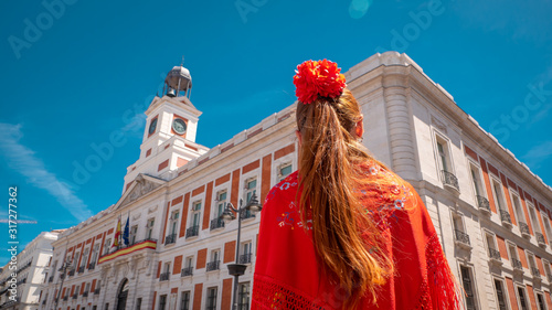 A young caucasian woman chulapa with red flower, traditional dress, and Spanish scarf at Puerta del Sol during San Isidro, the spring festival in May in the downtown of Madrid, the capital of Spain photo