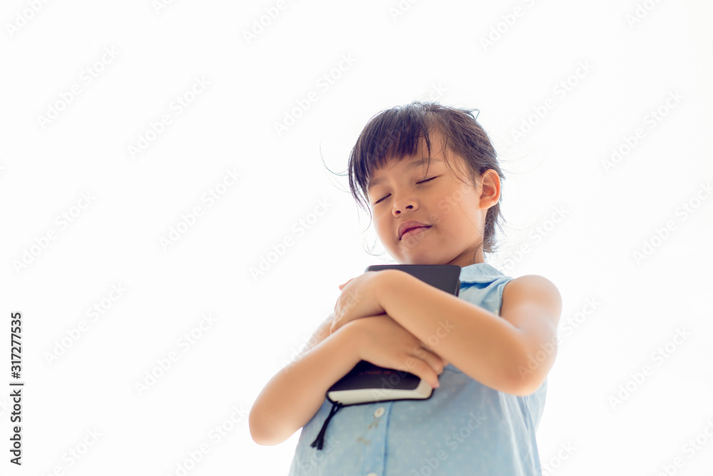 Asian little girl close her eyes holding bible book hands folded praying on white bacground Asian little girl close her eyes holding bible book hands folded praying on white bacground