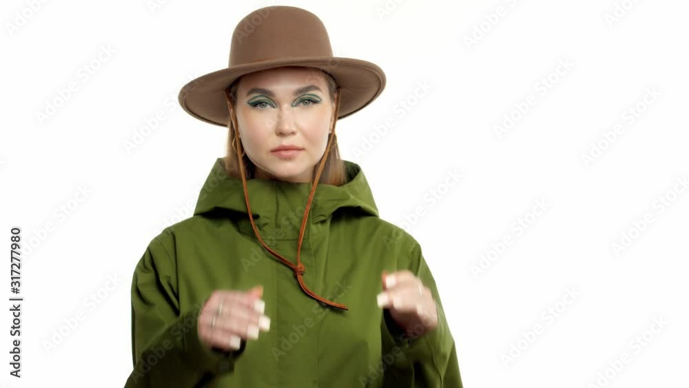 Caucasian woman in a autumn look in studio in khaki parka and hat turns and poses to the camera touches her face and hat Caucasian woman in a autumn look in studio in khaki parka and hat turns and poses to the camera touches her face and hat