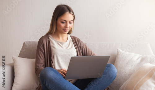 Charming millennial girl typing on laptop at home