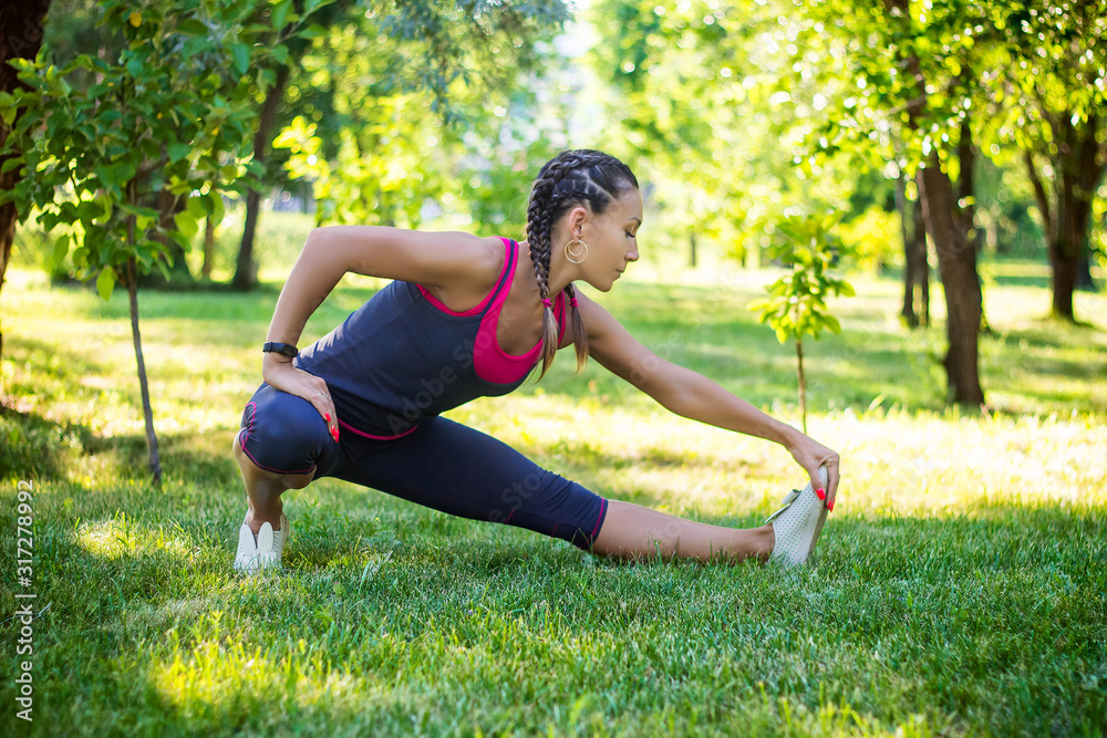 Sports woman doing exercises for stretching the legs, sits on the splits. In the park on the lawn. Sports woman doing exercises for stretching the legs, sits on the splits. In the park on the lawn.