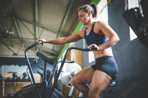 Female fitness model exercising on an elliptical training bike in a gym