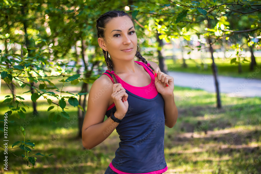 Athletic woman stands in the park on a background of trees Athletic woman stands in the park on a background of trees