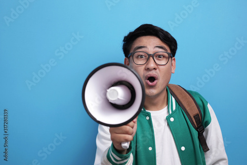 Young Asian male student wearing green baseball jacket shouting on megaphone