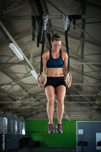 Female fitness model doing cross fit training on over head rings in a gym by pulling herself up © Dewald