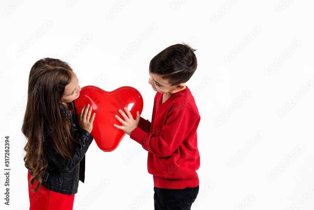 Happy little couple girl and boy holding red heart balloon together isolated on white background. children look at each other. St. Valentine's Day Happy little couple girl and boy holding red heart balloon together isolated on white background. children look at each other. St. Valentine's Day