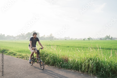 Asian young male wear helmets to ride folding bikes in the rice fields in the morning