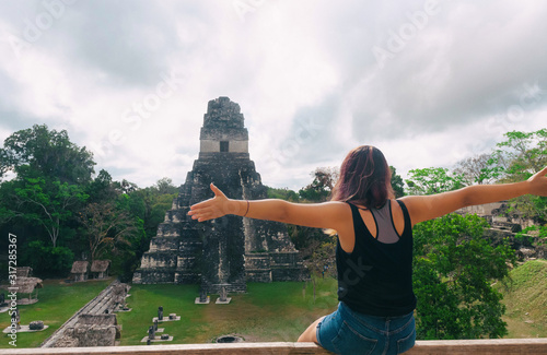 woman with open arms sitting in front of a pyramid in tikal national park in guatemala