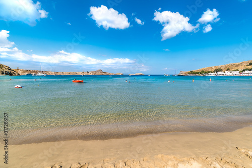 View of sandy beach and people in sea in Bay of Lindos, clouds on blue sky (Rhodes, Greece)