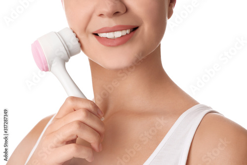 Young woman washing face with cleansing brush on white background, closeup. Cosmetic product