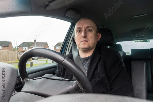 A middle aged man sat in the driving seat of a car.