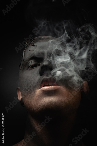 Close-up portrait of a handsome guy in makeup blows smoke. Stock art photo of a smoker. photo
