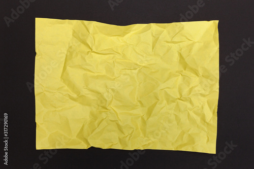 Crumpled piece of yellow paper with copy space on a black paper background. Top view.