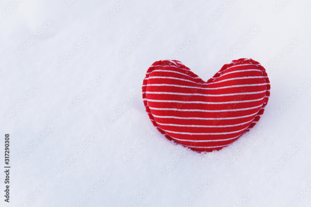 Homemade textile soft heart of red color with white stripes on the cold snow in winter.  Selective focus. A gift for Valentine's day. Lonely heart