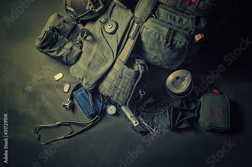 The backpack of a military medic stands on a green background. Around lies a first aid kit and various doctor tools. View from above.
