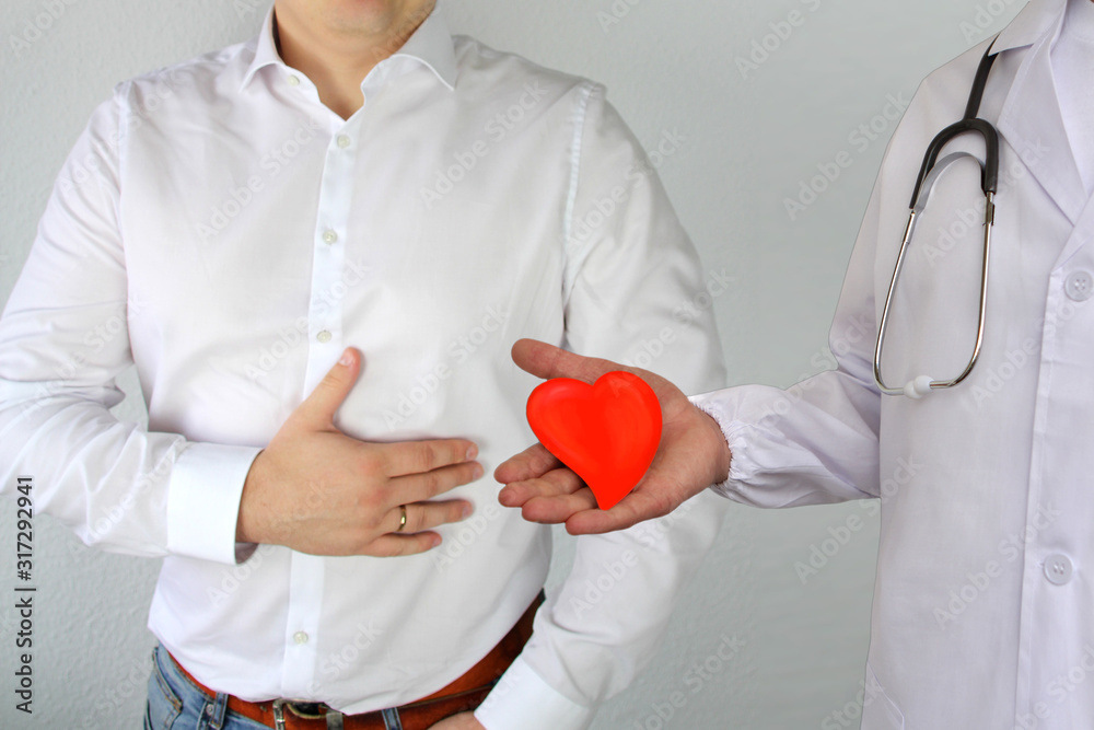 man in a white shirt holds on to his chest in the heart area, next is a doctor in a white coat and red heart model, concept of health problems, heart disease, surgery, organ transplantation man in a white shirt holds on to his chest in the heart area, next is a doctor in a white coat and red heart model, concept of health problems, heart disease, surgery, organ transplantation