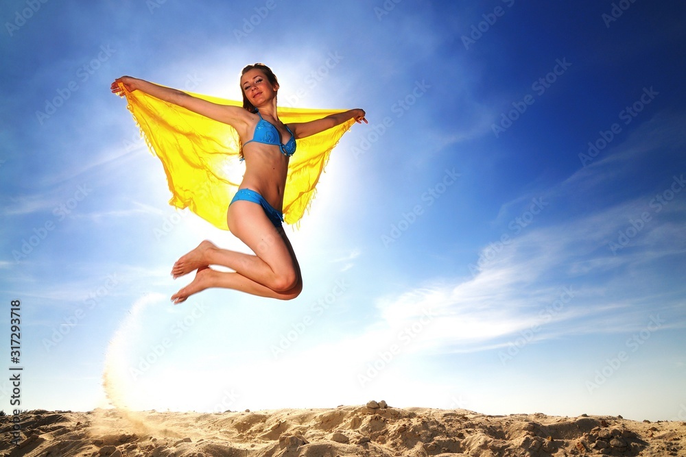 Young woman in bikini jumping over sand with umbrella in hands Young woman in bikini jumping over sand with umbrella in hands