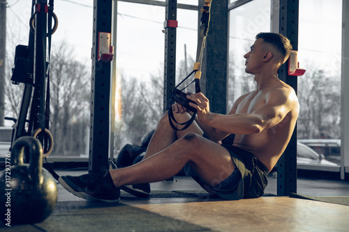 Resting. Young muscular caucasian athlete training in gym, doing strength exercises, practicing, work on his body. Taking break in trainings. Fitness, wellness, sport, healthy lifestyle concept.