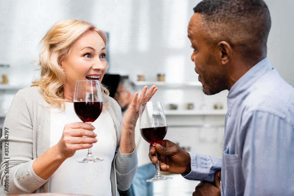 smiling woman and african american man talking and holding wine glasses