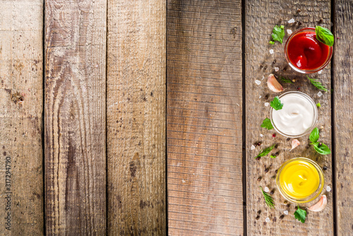 Set of sauces in small bowls - ketchup, mayonnaise, mustard, bbq sauce, pesto, classic burger sauce, with spices and herbs in. Wooden background copy space top view