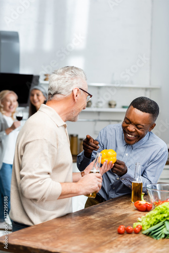 smiling african american man pointing with at his friend with bell pepper