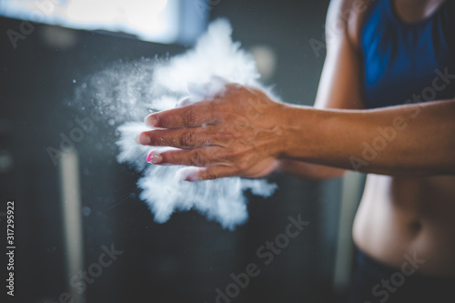 Female fitness model clapping hands with talcum powder in a gym before weight training