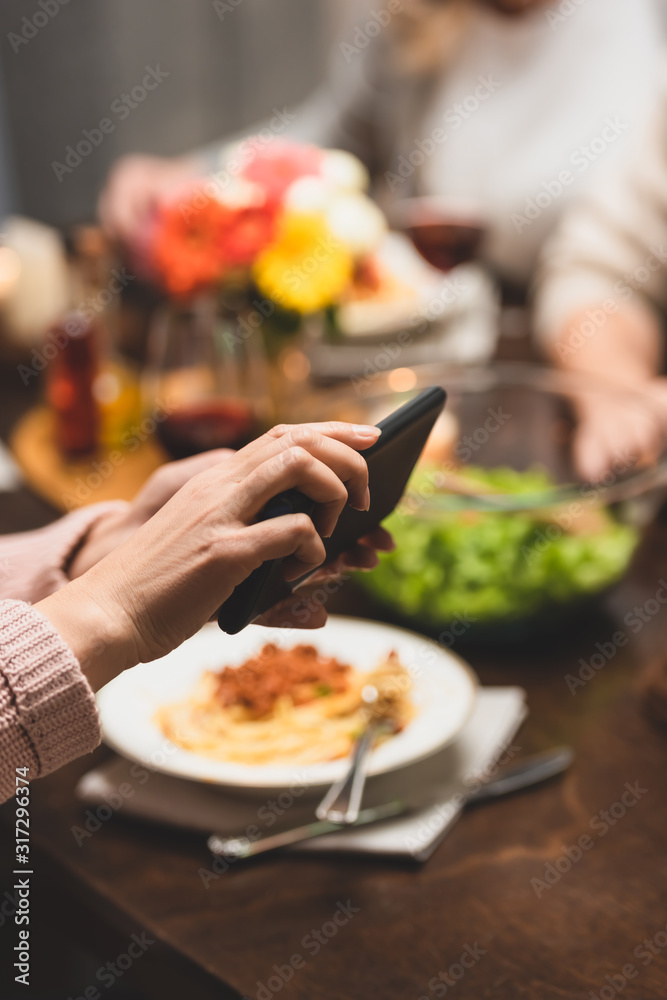 cropped view of woman holding smartphone during dinner
