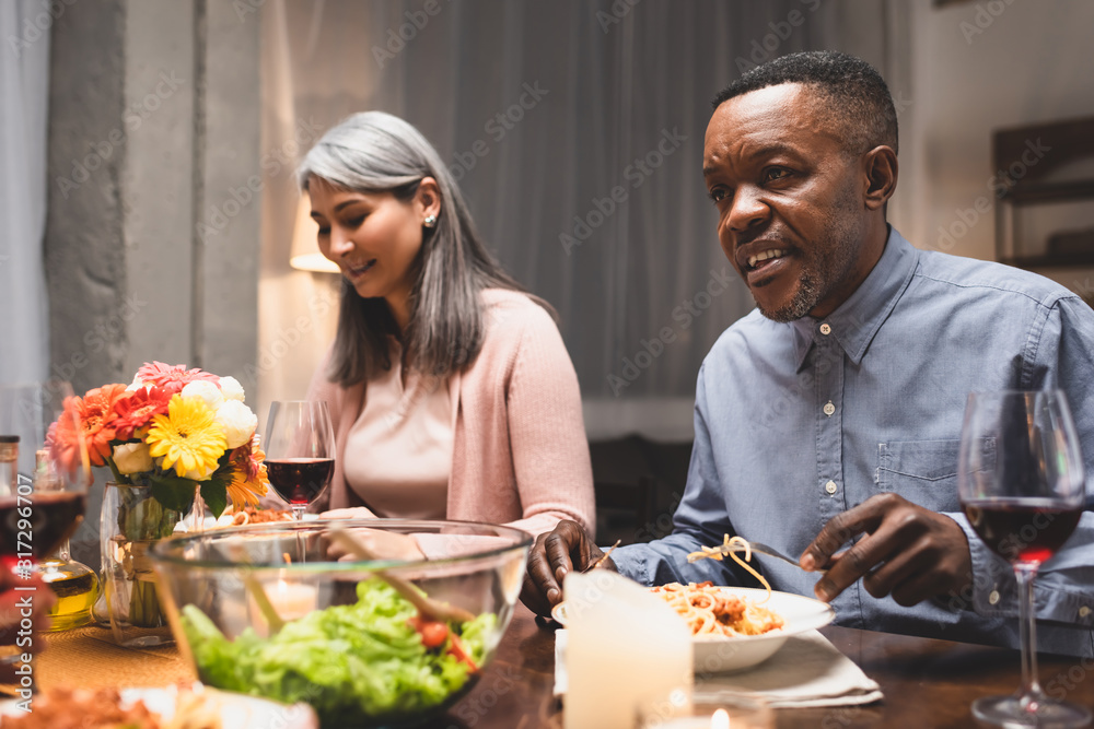 smiling multicultural friends talking and sitting at table during dinner smiling multicultural friends talking and sitting at table during dinner