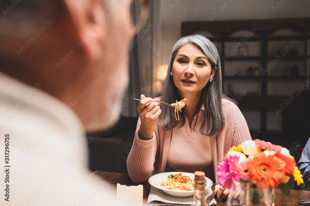 selective focus of asain woman eating pasta and looking at friend during dinner