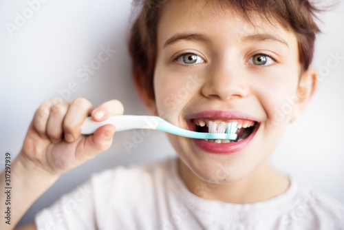 Closeup horizontal portrait of smiling child brushing teeth with blue and white toothbrush. Dental and health care from childhood. Healthy changing teeth on smiling face. White background. Copy space