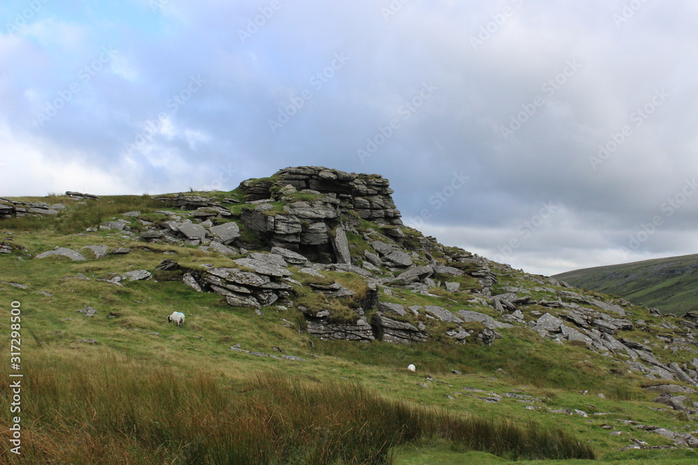 Photo of a landscape depicting a view of green hills and rocks against a blue sky with clouds in the Dartmoor National Park located in the UK Photo of a landscape depicting a view of green hills and rocks against a blue sky with clouds in the Dartmoor National Park located in the UK