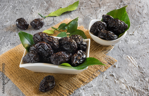 bowl of sweet dried plums with lemon leaves on rustic stucco background photo