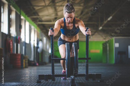 Female fitness model pushing a sled in a cross fit gym.
