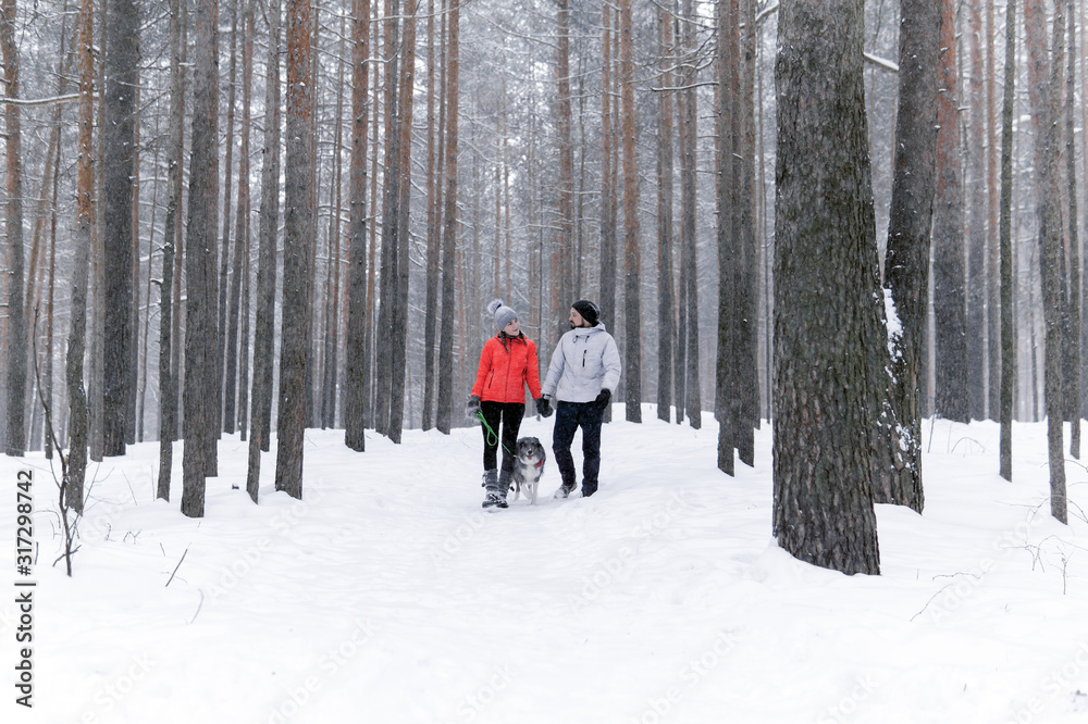 young couple walking a dog in the winter forest